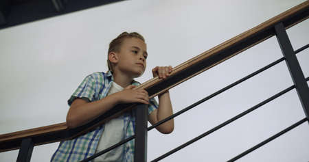 Curious school child standing stairway alone at break. Preteen schoolboy leaning on railings examine...