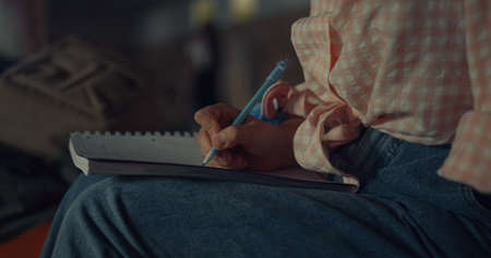 Girl hands writing thoughts in notebook holding pen close up. Unrecognized stylish teen student doing art homework in sketchbook. Schoolgirl sitting couch school hallway alone. Teenagers lifestyle.の写真素材