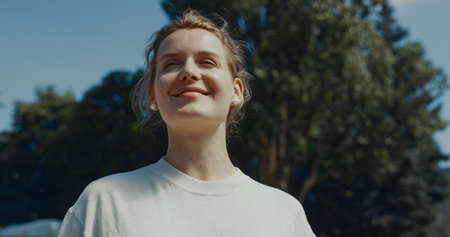Portrait of joyful woman standing waving in summer sunlight. Young beautiful parent saying goodbye watching outdoors. Pretty blonde mom enjoying morning time close up. Mothers support concept.の写真素材