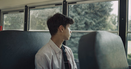 Thoughtful Indian teenager boarding on schoolbus. School boy with broken arm take seat alone. Tired dark-haired student holding backpack looking in window. Hand wrapped in cast. Education concept.の写真素材