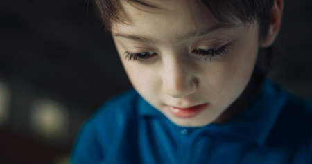 Portrait of serious pupil watching tablet screen surfing internet on school break. Focused elementary age boy playing online game using pad computer in campus. Children technology addiction concept.の写真素材