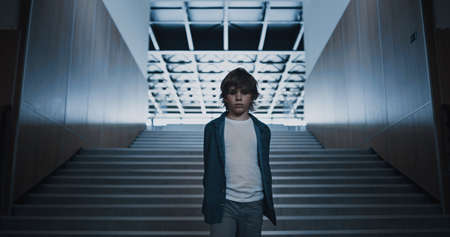 Sad little boy walking empty modern school hall. Unhappy elementary age schoolboy feel depressed...
