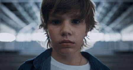 Portrait of elementary age boy standing alone full of despair in abandoned hall. Depressed preteen...