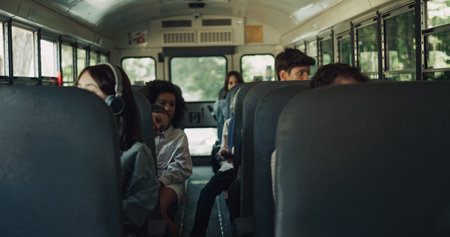 Diverse students sitting schoolbus together. Multiracial teenagers going home after study. Group of multi ethnic school children riding in academic shuttle. Public education transportation concept.の写真素材