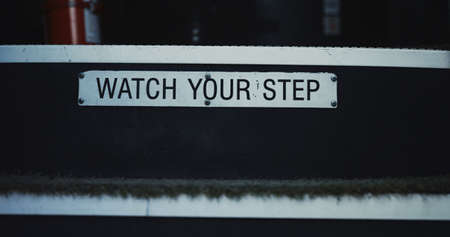 Watch your step warning sign school bus for children attentiveness safety closeup. Metal plate with inscription on stairway students transport. View of open schoolbus entrance with stairs inside cabinの写真素材