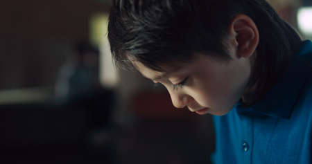 Dependent little schoolboy surfing social media communicating with friends using tablet close up. Obsessed boy play online games alone on school break. Focused teen guy ignore classmates in hallway.の写真素材