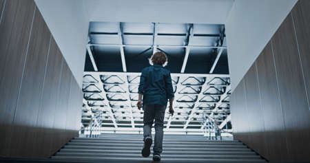 Relaxed teenager silhouette going upstairs alone on bright light. Unrecognizable teen student walking modern empty stairway after classes. Lonely schoolboy wandering in school building back view.の写真素材