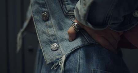 Close up girl hand wearing ring on hips. Unrecognized stylish schoolgirl pose in blue jeans clothes standing at lockers. View of teenage denim look with metallic buttons. Teen outfit concept.の写真素材