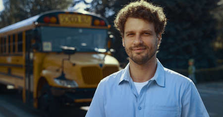 Smiling man driver posing near yellow academic vehicle alone close up. Joyful professional schoolbus...