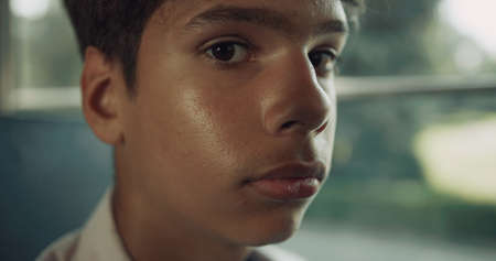 Portrait of sad Indian school boy looking camera in students vehicle. Thoughtful dark-haired pupil...