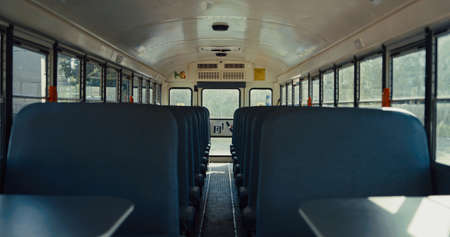 Empty comfortable seats placed schoolbus interior during daytime close up. Free aisle in modern public vehicle. Inside saloon parked school bus without passengers. American safety transport concept.の写真素材