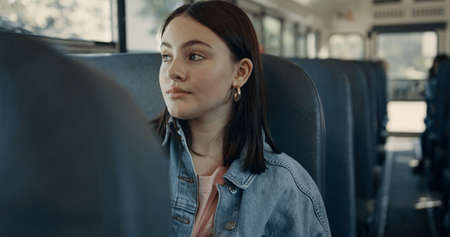 Focused teenage girl sitting in empty schoolbus alone. Cute tensed student looking window on daily...