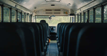 Empty aisle black seats in modern schoolbus. Comfortable bus interior without passengers closeup. View inside saloon driver cabin in safety public transport. No children in parked school autobus.の写真素材