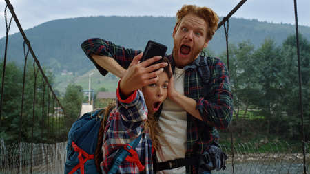 Friends taking selfie photo on smartphone. Tourists couple grimacing at mountains nature. Cheerful...