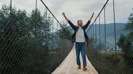 Carefree guy explore nature on mountains river bridge. Excited hiker walk outdoors on active...