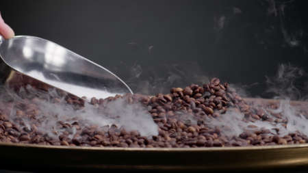 Metal scoop mixing roasting coffee beans close up. Unknown man hand holding shovel gathering brown...