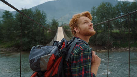 Excited traveler enjoy landscape nature mountains. Closeup joyful hiker walk on river bridge. Curious man spend summer trip on holiday vacation. Smiling backpacker look around woods. Travel concept.の写真素材