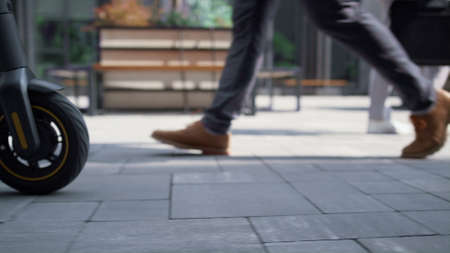 Closeup girl legs walking with electric scooter. Modern city transportation. Unrecognized girl...