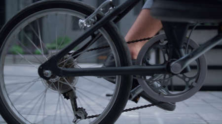 Closeup male legs pedaling city street in black shoes. Unrecognized man startup ceo riding bicycle...