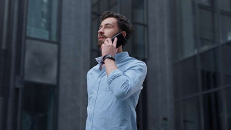 Attractive businessman making phone call at modern building. Successful manager bearded brunet man...