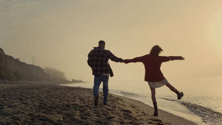Back view loving couple walking on sandy beach. Happy girl and guy enjoying summer sunset at sea....