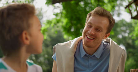 Munching boy laughing talking with happy father on picnic close up. Cheerful family have curious...