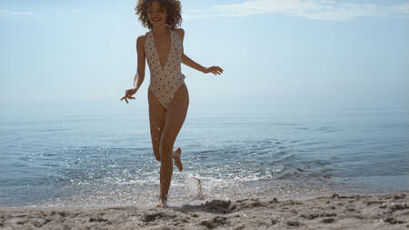 Happy attractive woman coming out ocean splashing water on summer vacation. Curly carefree girl...