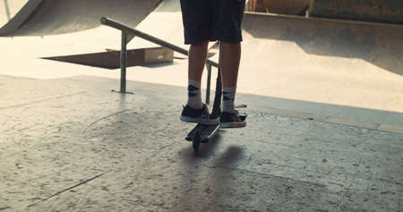Young scooter rider performing tricks on ramp at skate park. Close up unknown male hipster jumping...