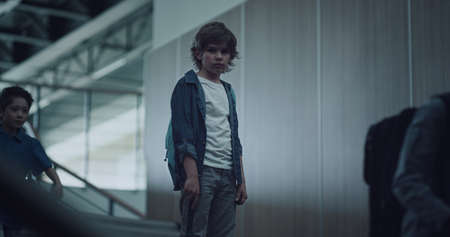 Sad little guy standing alone on school stairs looking ahead. Diverse pupils running downstairs...