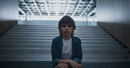 Stressed schoolboy stay alone on dark stairway close up. Depressed unhappy boy hiding in school...