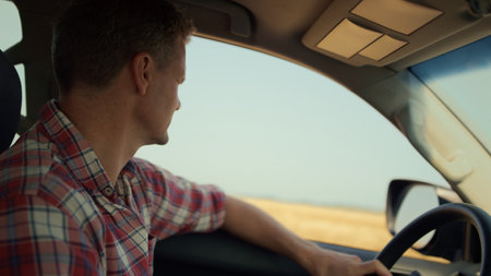 Man driving countryside inside vehicle closeup. Driver inspecting wheat field looking suv window on...