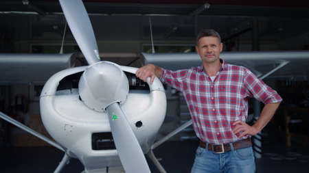 Pilot airplane posing standing hangar leaning on white aircraft body with propeller close up. Happy...