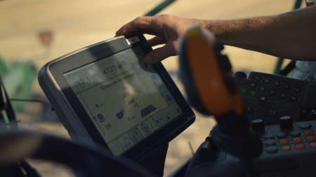 Hand touching harvester monitor closeup. Tractor driver working grain field in sunlight....