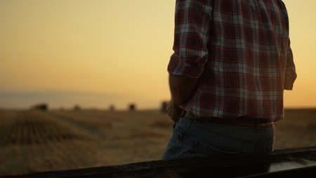 Unknown farmer owner looking haystack wheat field after harvesting at sunset farmland. Unrecognizable man agronomist worker inspect examine dry bale at morning sunrise. Modern farming concept.の写真素材