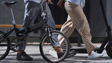 Workers legs walking downtown with electric scooter bicycle in hands close up. Unrecognized corporate people man woman commute office on green city transport. Managers use shared two-wheeled vehiclesの写真素材