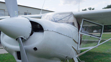 Small private plane parked on green grass aerodrome cloudy day close up. White ultralight airplane...