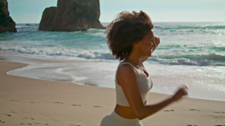 Happy african american woman running on sandy beach beautiful summer morning. Active cheerful girl...