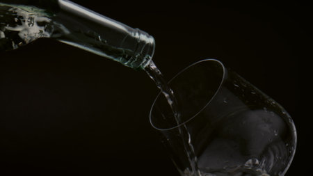 Mesmerizing view of pouring golden wine from bottle to clear goblet on black background close up. Stream yellow alcohol drink flowing to wineglass in super slow motion. Gourmet beverage concept.の写真素材