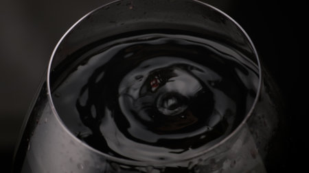 Red wine droplet falling transparent wineglass in super slow motion closeup. Smooth alcohol drink surface ripple in circles top view. Delicious grape beverage waving inside goblet on black background.の写真素材