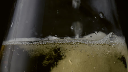 Golden tasty champagne drip in clear wineglass closeup. Sparkling wine droplets falling on liquid surface making bubbly foam. Fizzy alcohol drink sizzling on black background. Gourmet beverage partyの写真素材