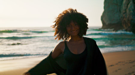 Cheerful woman flirting on camera walking sand beach at sunrise close up. Happy african american girl smiling playfully enjoying summer stroll on seashore. Joyful lady rest on nature morning time.の写真素材