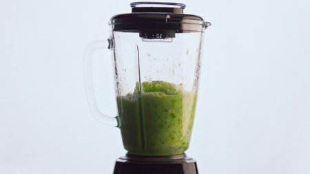 Blending green vegetable smoothie in electric mixer close up. Fresh organic blend from veggies herbs...