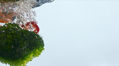 Fresh vegetable fall clear water with splashes in super slow motion close up. Tasty vitamin veggies dropped underwater on white background. Organic broccoli pepper carrot cauliflower in liquid.の写真素材