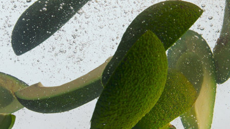 Closeup tasty sliced avocado in clear liquid at white background. Ripe green pieces fresh vegetable floating in transparent water with bubbles super slow motion. Healthy vitamin food for vegetarian.の写真素材