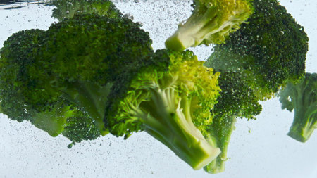 Closeup green broccoli underwater on white background. Fresh ripe pieces cabbage floating clear...