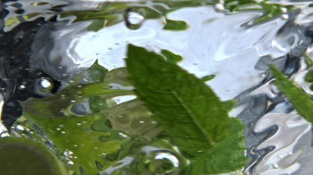 Fizzy mint cocktail rotating inside clean glass closeup. Sparkling vitamin water with drops spinning...