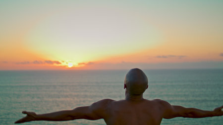 Yogi silhouette practicing asana in beautiful sunset. Strong man relaxing alone rising hands in at ocean sunrise. Unknown muscular athlete concentrating meditate at sea. Serene stress free concept.の写真素材