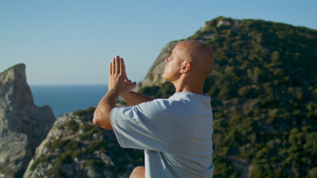 Athletic man practicing yoga on cliff edge sunlight. Beautiful ocean landscape in summer. Focused handsome man meditating rising hands at stunning sea view. Mindfulness lifestyle asana balance conceptの写真素材