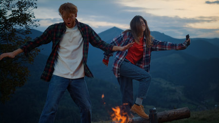 Happy couple dance evening in mountains nature. Tourist family have fun outside close up. Carefree lovers jump by bonfire at sunset evening. Young travelers have fun on active trip. Leisure concept.の写真素材