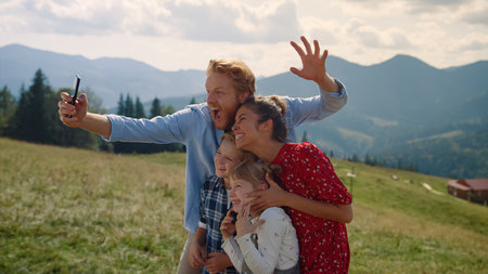 Funny family fooling making selfie standing on summer mountains side view. Cheerful couple with two...
